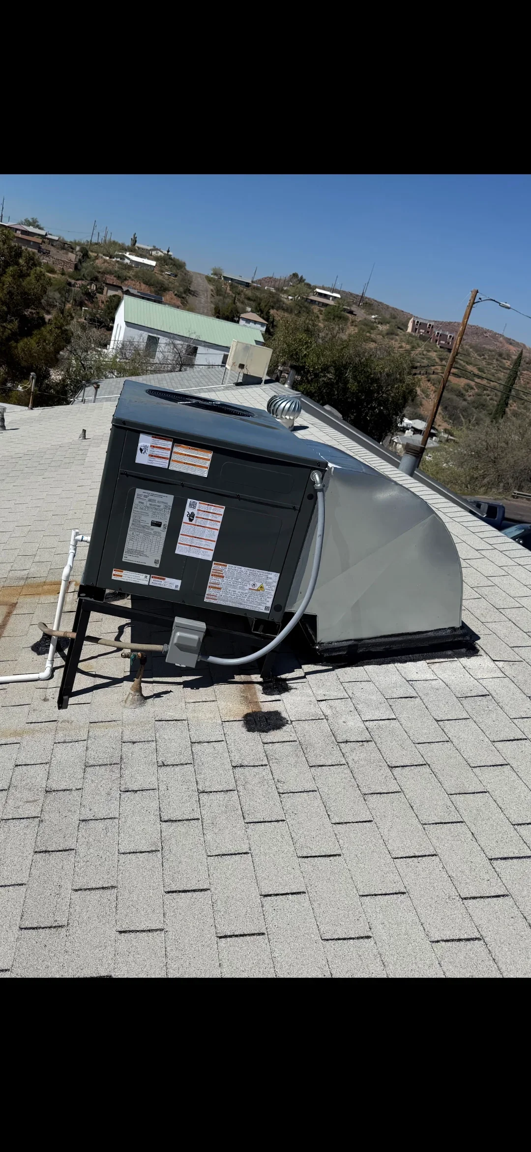 Rooftop AC unit installation on asphalt shingle roof with black condensing unit and mounting hardware