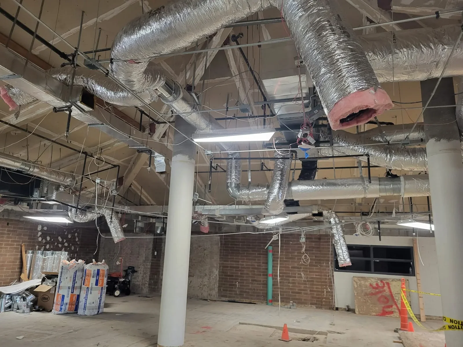 Flexible insulated ductwork with pink wrap and metal ducts installed in commercial ceiling space