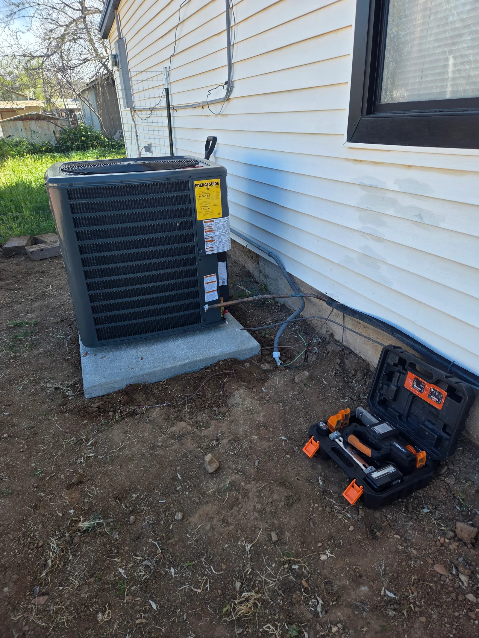 New AC condenser unit on concrete pad with refrigerant lines and electrical connections