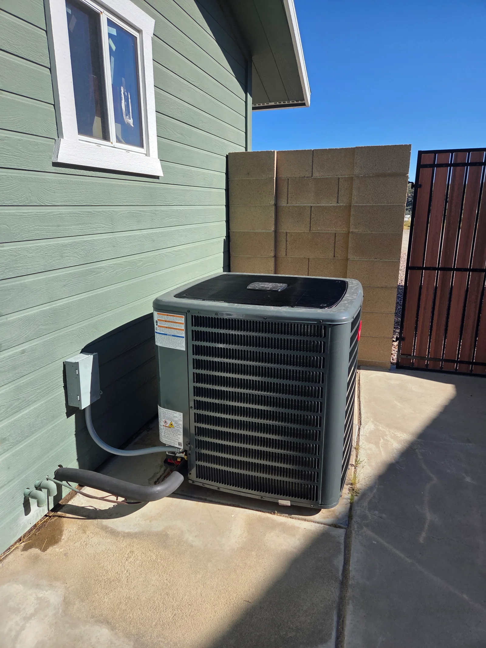 New AC condenser unit installed on concrete pad with refrigerant lines and electrical connections
