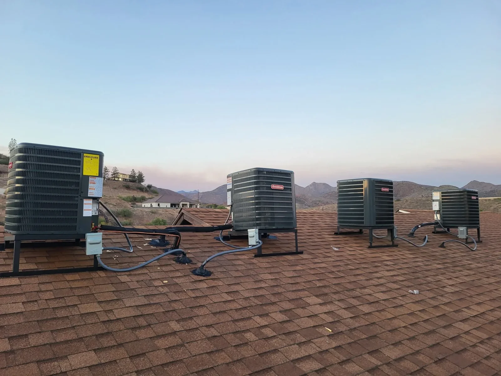 Four rooftop AC units installed on asphalt shingle roof with electrical connections and metal mounting brackets