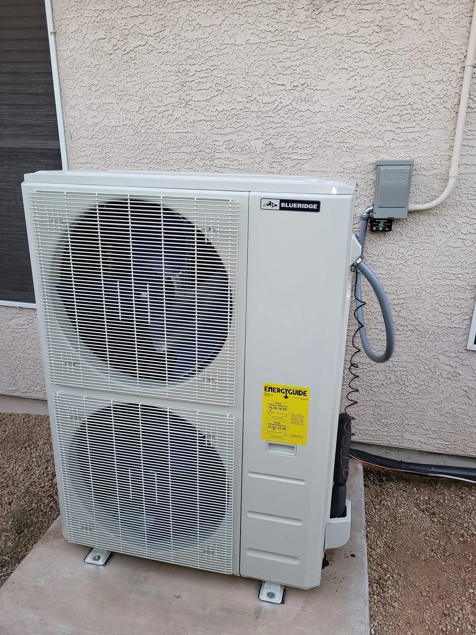 Blueridge heat pump condenser unit installed on concrete pad with electrical disconnect and refrigerant lines