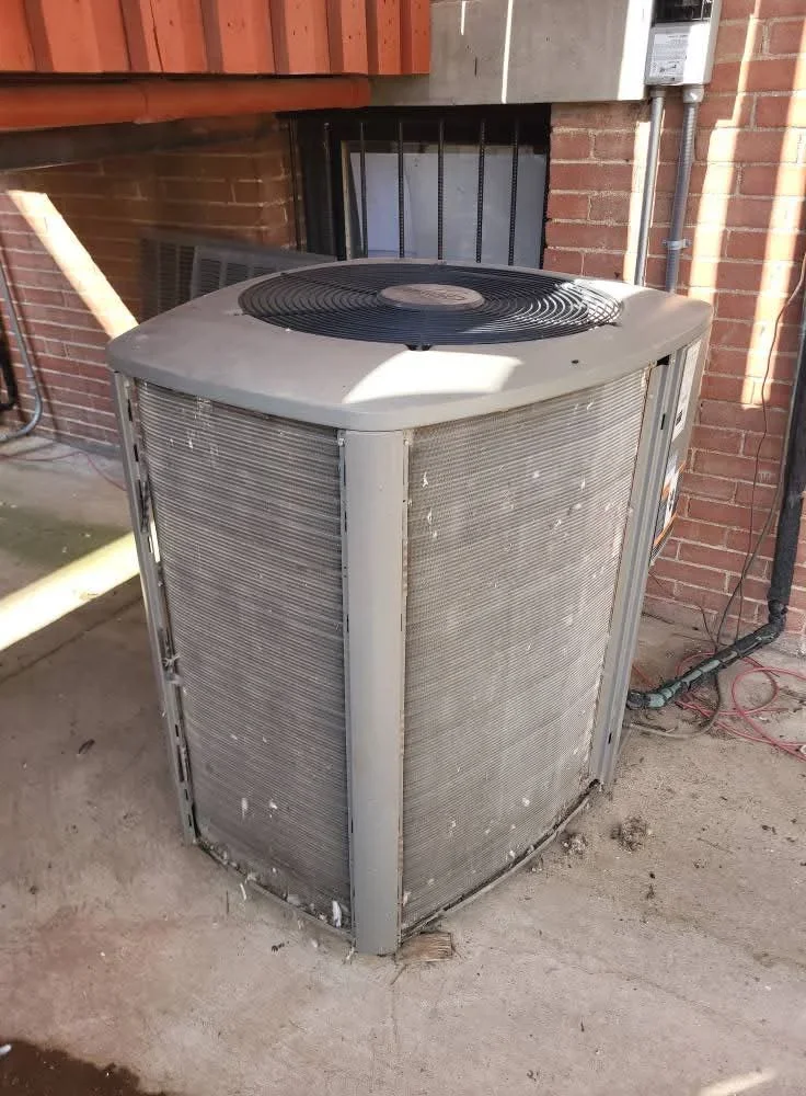 New central AC condenser unit with gray cabinet and black fan motor on concrete pad