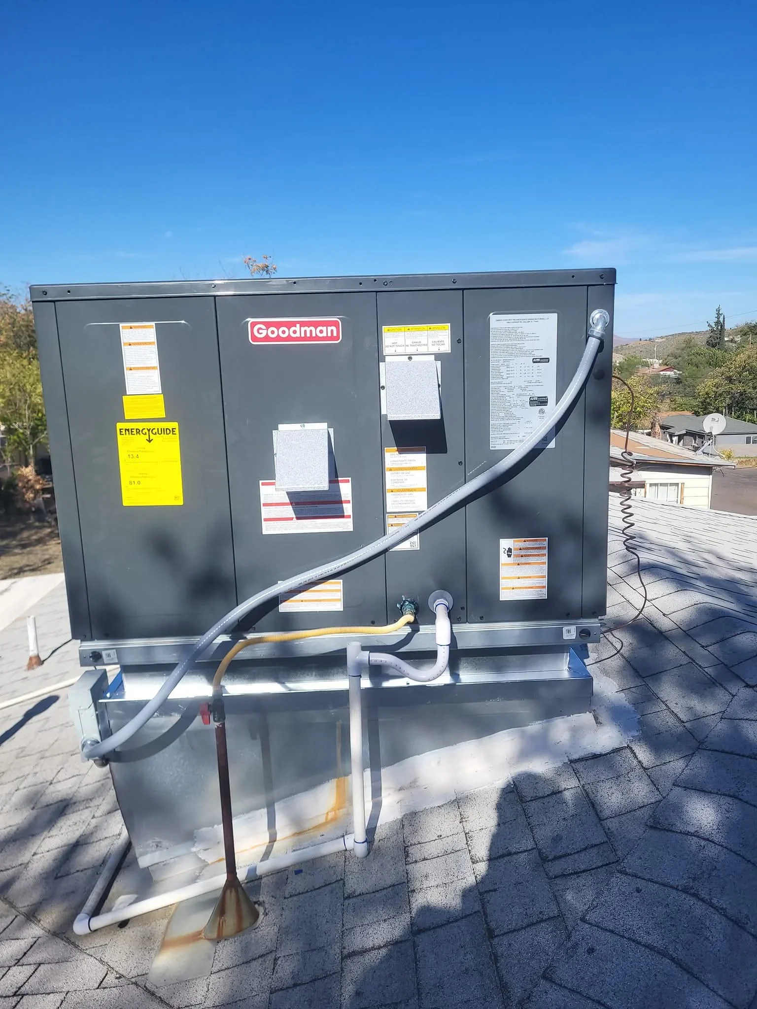 Goodman AC unit installed on roof with refrigerant lines, condensate drain, and electrical connections